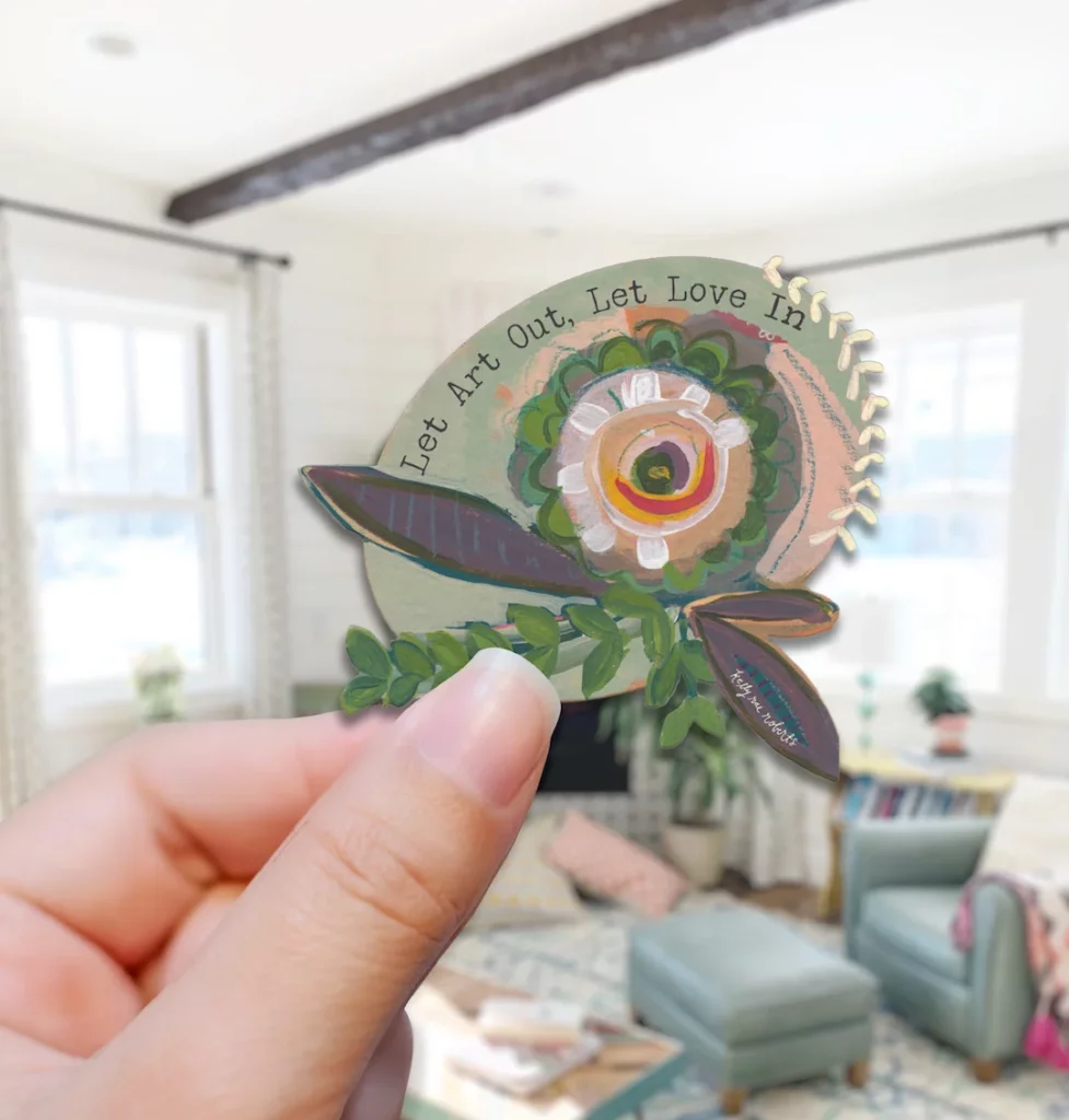 Hand holding a sticker with motto: Let Art Out