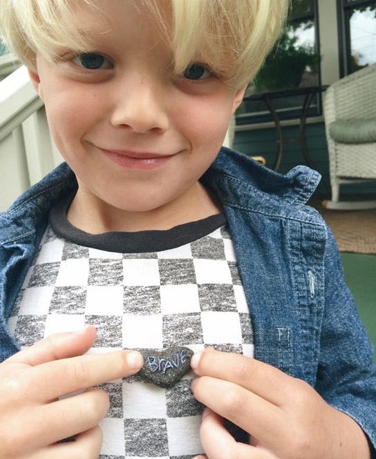 True, the son of mixed media artist Kelly Rae Roberts, holding a heart-shaped rock with the word brave written on it
